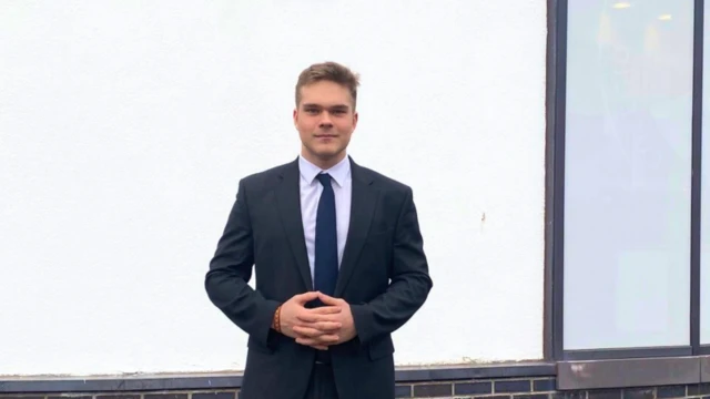 7b336970-def7-11ef-98f2-fb6004d12416-png Illia in a dark suit standing outside his school.